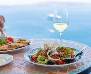 Fresh Greek salad with feta cheese, olives, and white wine on a mosaic table at a seaside restaurant in Athens, Greece.