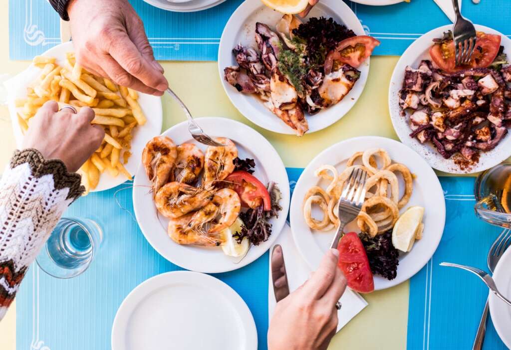 table full of food at lunch - marine fish and healthy food - above and top view - some hands taking food from the middle of the table
